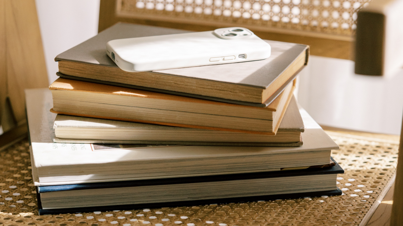 Stack of books with a smartphone on top, placed on a woven surface.