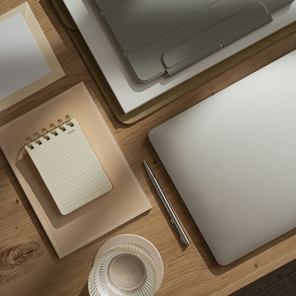 Desk setup with a laptop, notebook, pen, and small decorative item on a wooden surface.