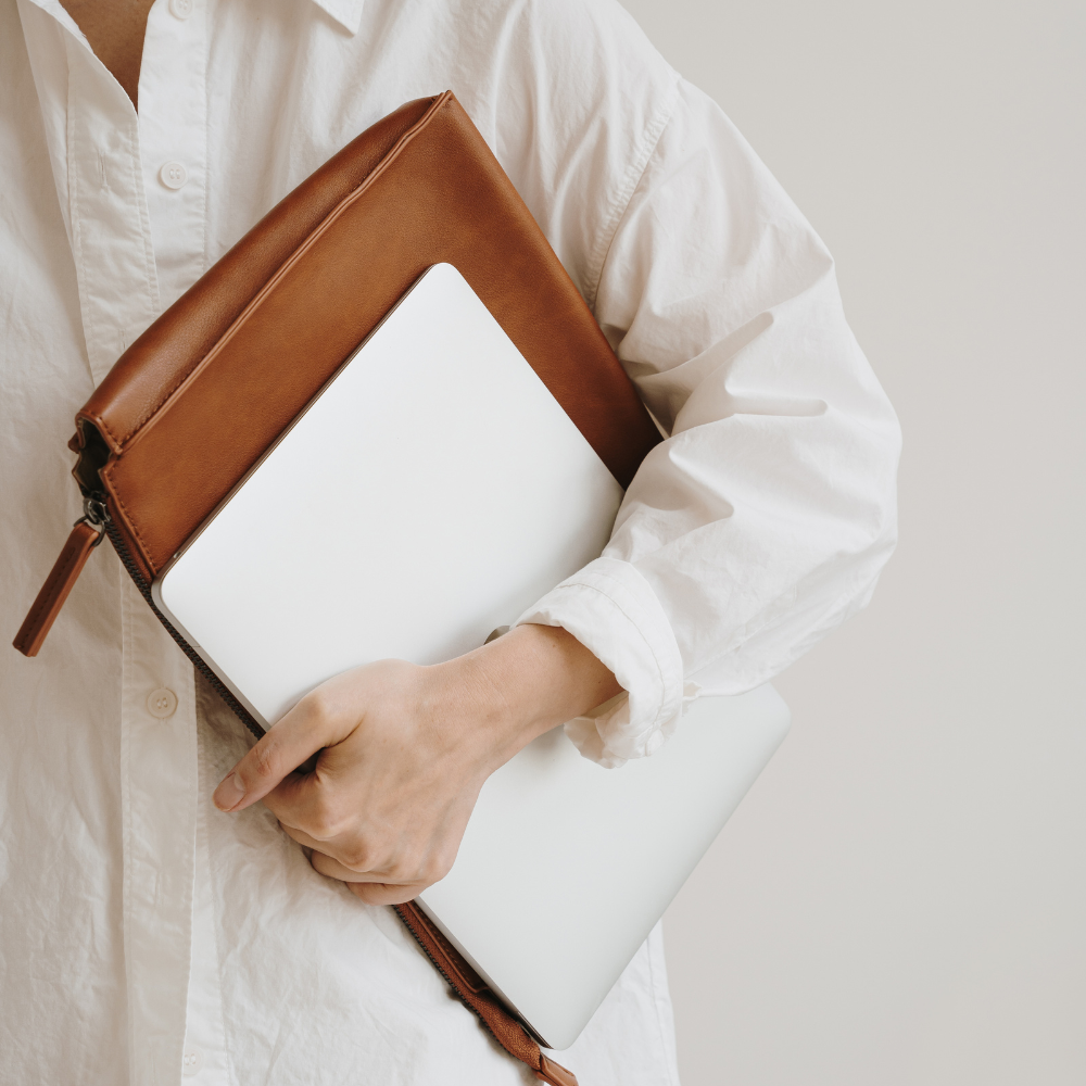Person holding a brown leather clutch with a white interior against a neutral background
