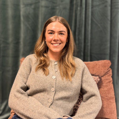 Woman wearing a gray sweater sitting on a brown chair with a dark curtain background