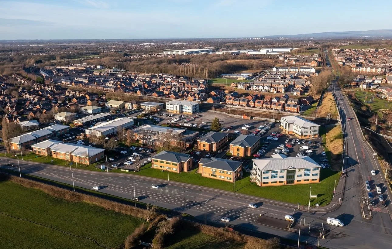 Aerial view of a suburban area with roads, buildings, and green spaces.