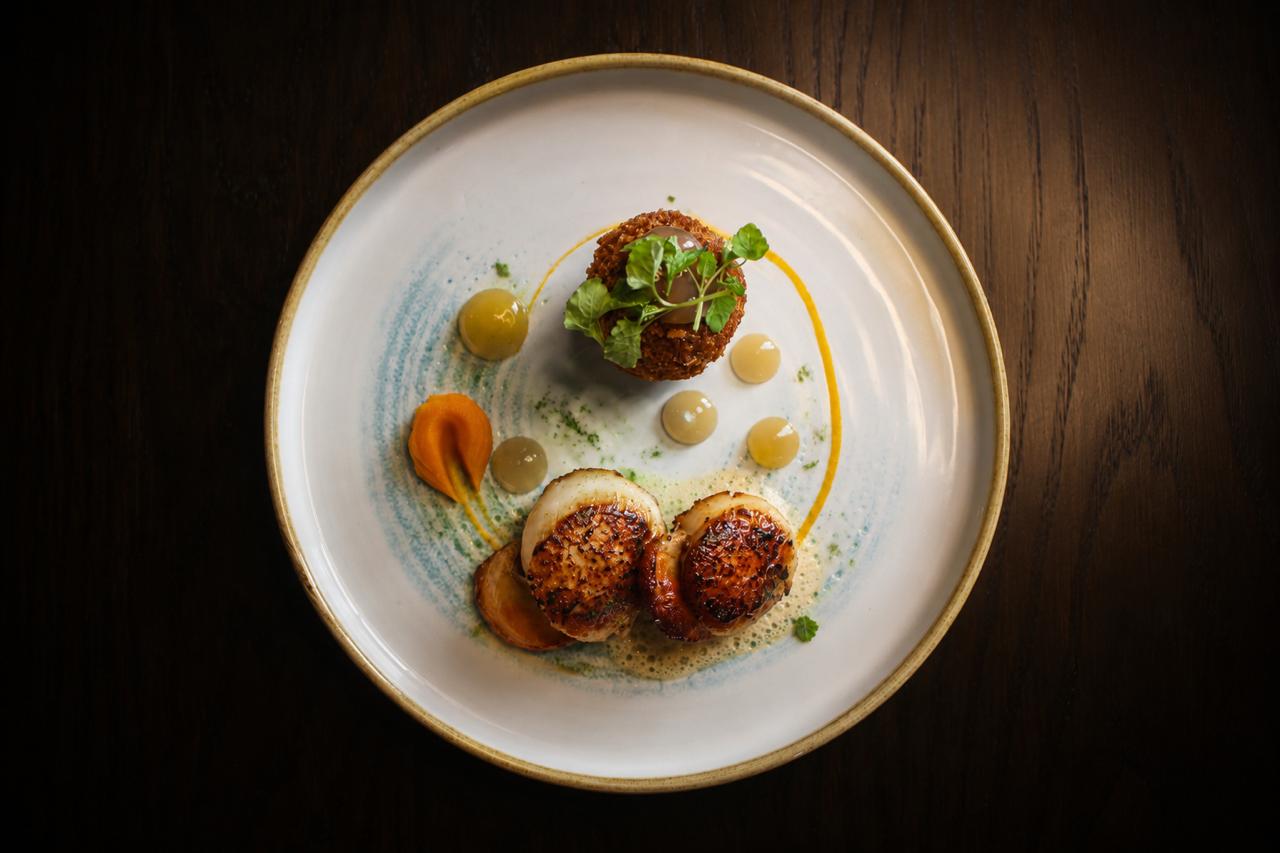 Plated dish of scallops with garnishes on a dark wooden table
